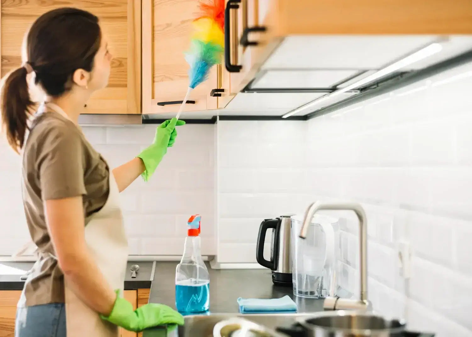 Woman cleaning kitchen cabinets with a duster for a healthier home environment