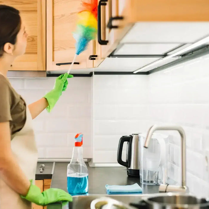 Woman cleaning kitchen cabinets with a duster for a healthier home environment