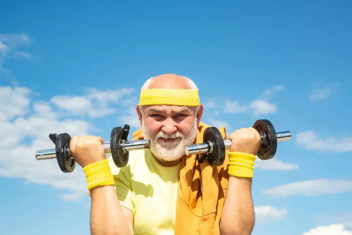 Older man exercising with dumbbells outdoors under a blue sky, representing vitality and health benefits of Tongkat Ali.
