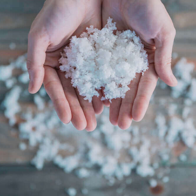Hands holding premium hand-harvested Celtic sea salt with scattered crystals on a wooden table.