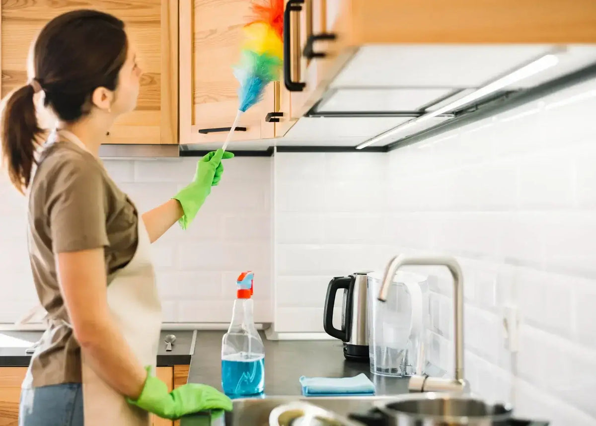 Woman cleaning kitchen cabinets with a duster for a healthier home environment