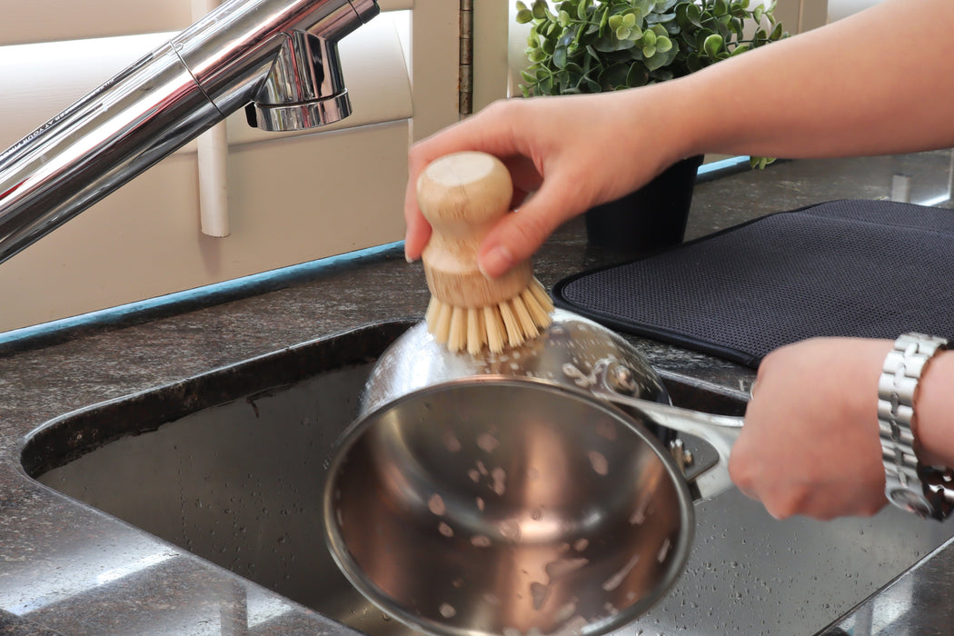 White Magic Eco Basics Plastic Free Pot Brush held in one hand while cleaning a saucepan