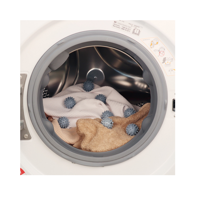Laundry dryer with White Magic Eco Basics balls amidst towels, showcasing efficient drying and fabric softening.